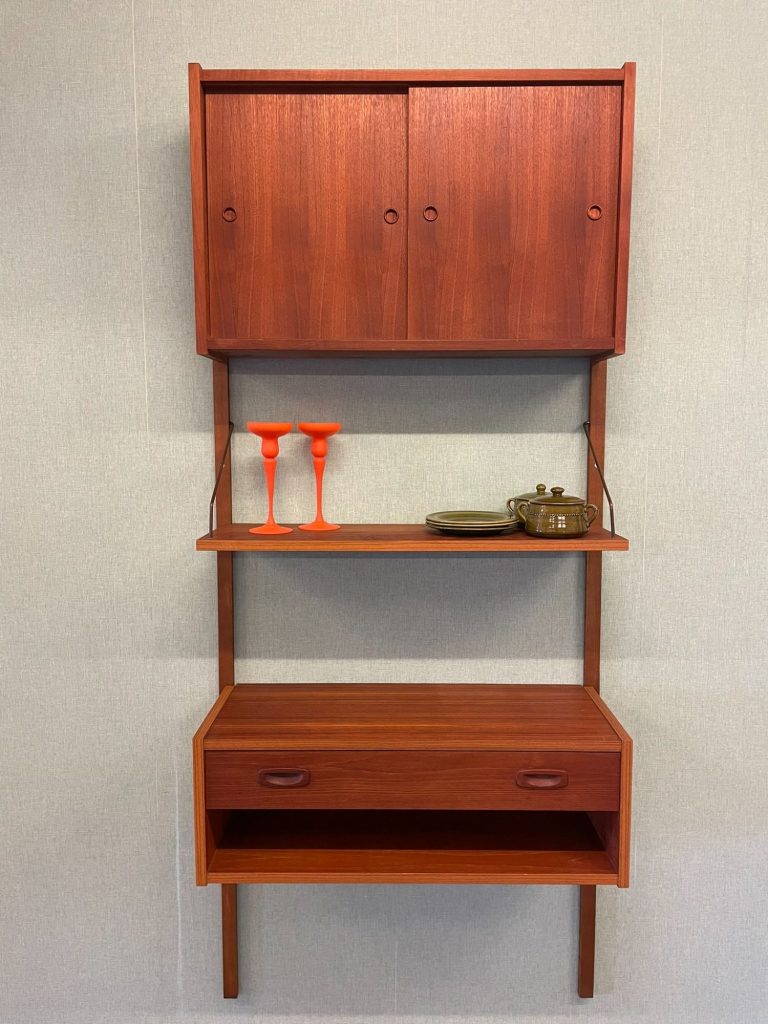 Wanndkast met twee deuren, een lade en decoratieve items op de planken.