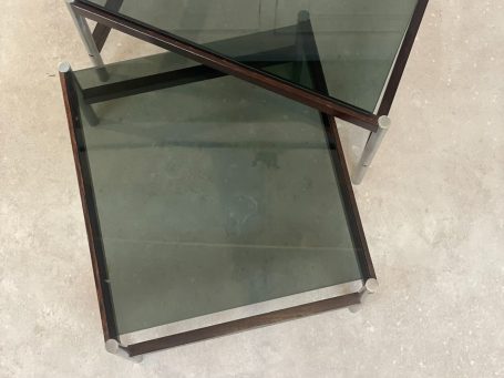 Twee glazen tafels met zwarte metalen frames, schuin op elkaar geplaatst.