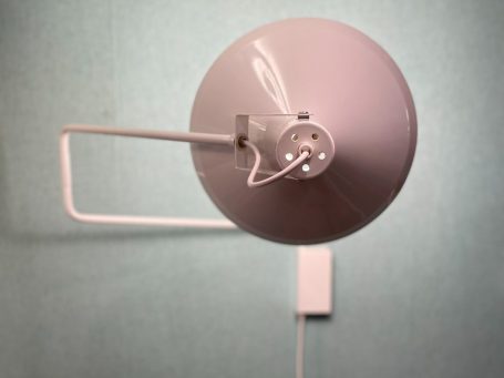 Een witte wandlamp aan een wand, met een lange arm en een schakelaar.